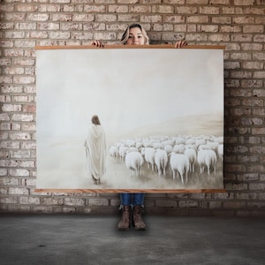 May include: A large canvas print depicting a religious scene with a figure in white robes walking towards a flock of white sheep. The scene is set against a hazy, light background.
