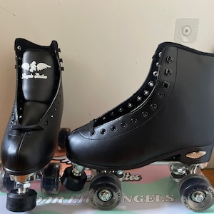 May include: Pair of black roller skates with white wings logo on the side. The skates have black wheels and silver trucks.