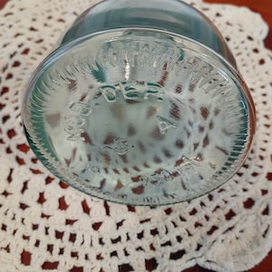 Op de afbeelding: Close-up van de bodem van een heldere glazen pot met een groene tint. De pot heeft een verhoogde rand en de woorden "MADE IN GERMANY" zijn in reli&euml;f op de bodem aangebracht.