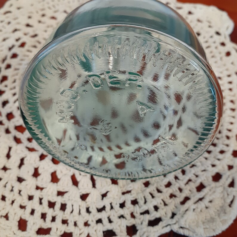 Op de afbeelding: Close-up van de bodem van een heldere glazen pot met een groene tint. De pot heeft een verhoogde rand en de woorden "MADE IN GERMANY" zijn in reli&euml;f op de bodem aangebracht.