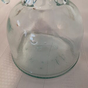 Op de afbeelding: Een heldere glazen fles met een getextureerd oppervlak. De fles heeft een brede opening en een afgeronde bodem. De fles is leeg.