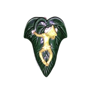 May include: A ceramic wall planter shaped like a green leaf with a small yellow fairy figurine climbing up the leaf.