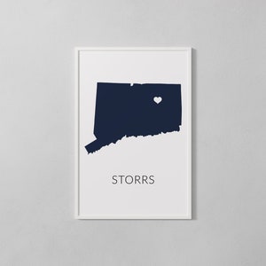 May include: A white framed print with a navy blue silhouette of the state of Connecticut. A white heart is placed in the center of the state. The text "STORRS" is printed below the state.