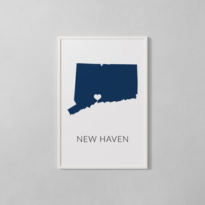 May include: A white framed print with a blue silhouette of the state of Connecticut with a white heart in the center of the state. The text "NEW HAVEN" is printed below the silhouette.
