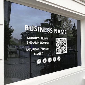 Op de afbeelding: Een zwart-wit bord met de tekst "BUSINESS NAME" in wit. Het bord bevat ook de openingstijden, "MONDAY - FRIDAY 9:00 AM - 5:00 PM", "SATURDAY - SUNDAY CLOSED", en een QR-code. Social media-iconen voor Facebook, Twitter, Instagram, Pinterest en Google zijn ook inbegrepen.