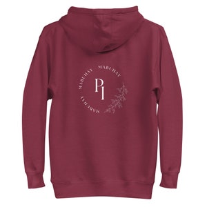 Puede incluir: Sudadera con capucha color burdeos con un logotipo circular blanco que dice "Mabuhay Club" y "PI" en el centro.