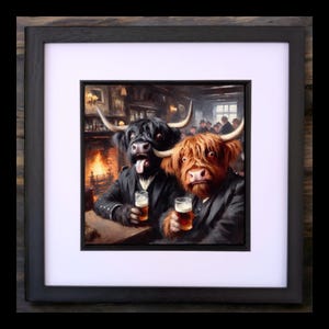 May include: A framed art print depicting two Highland cows in a pub, each with a pint of beer. One is black, the other ginger, both wearing jackets. The background shows a fireplace and other people. The artwork is framed in black.