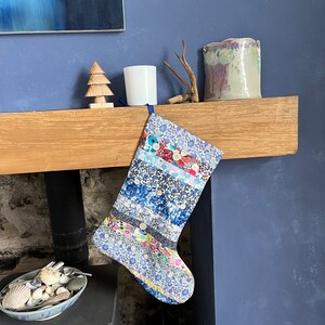 May include: A blue and white patchwork Christmas stocking with colourful buttons and a floral pattern hangs on a wooden mantelpiece.