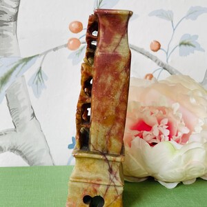 May include: A carved stone vase with a red, yellow, and green color scheme. The vase has a unique design with intricate details and a base with a decorative opening.