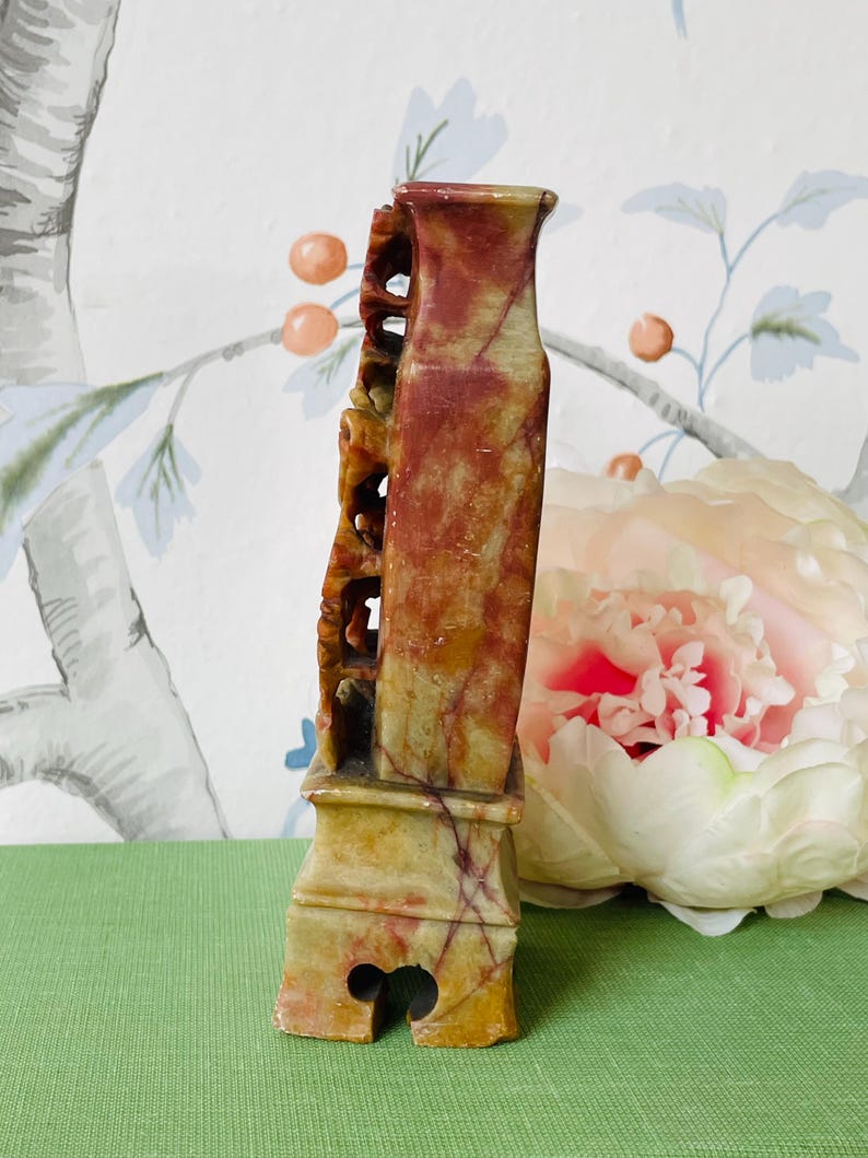 May include: A carved stone vase with a red, yellow, and green color scheme. The vase has a unique design with intricate details and a base with a decorative opening.