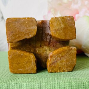 May include: A small, square, carved stone object with a reddish-brown color and a yellow-brown base. The base has four uneven, rounded feet.