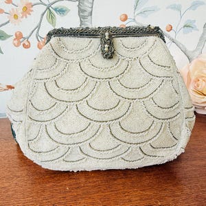 May include: Vintage ivory beaded handbag with a scalloped pattern. The purse has a silver-toned clasp and a beaded handle. The design is made of small, round beads, creating a textured, elegant look. The bag is likely from the mid-century era.