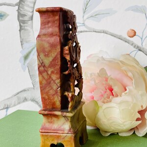 May include: A carved stone vase with a red, yellow, and green color scheme. The vase has a floral design and a square base.
