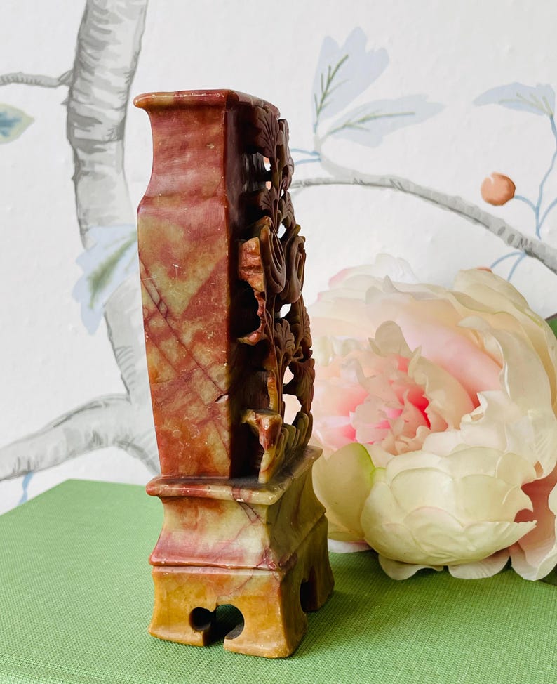 May include: A carved stone vase with a red, yellow, and green color scheme. The vase has a floral design and a square base.