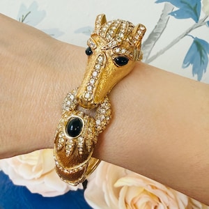 May include: Gold-toned horse head bracelet with clear crystal accents and black stone eyes. The horse head is adorned with sparkling crystals, and the bracelet features a hinged design. A unique piece of jewelry.