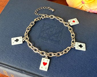 May include: Silver bracelet with playing card charms. The chain link bracelet has four small card charms and one larger charm. The card charms display the suits of hearts, spades, diamonds, and clubs.