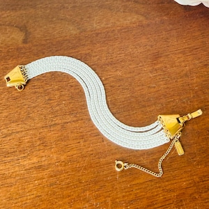 May include: A vintage silver-tone bracelet with a gold-tone clasp and accents. The bracelet features multiple flat, woven strands. The clasp is a gold-tone triangle shape. A small gold chain and tag hang from the clasp.