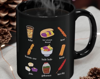 May include: Black coffee mug with a white design of various Filipino foods, including ice cream bread, halo halo, banana cue, turon, and more. The text below each food item identifies the food.