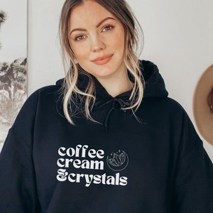 May include: Black hooded sweatshirt with white text that reads "coffee cream & crystals" and a small graphic of a crescent moon and stars.