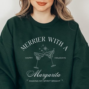 May include: A dark green sweatshirt with the text "Merrier with a Margarita Making my spirit bright" and a graphic of two margarita glasses clinking.