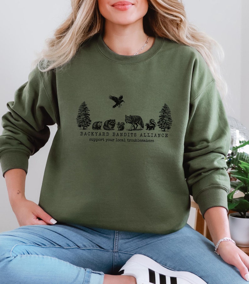 May include: A green sweatshirt with a black graphic print of a forest scene with animals and the text "Backyard Bandits Alliance support your local troublemakers".