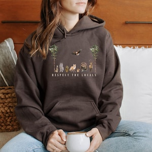 K&ouml;nnte beinhalten: Ein brauner Hoodie mit einem Aufdruck von Tieren in einem Wald mit dem Text "Respect the Locals".