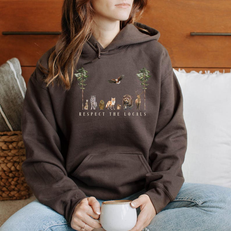 K&ouml;nnte beinhalten: Ein brauner Hoodie mit einem Aufdruck von Tieren in einem Wald mit dem Text "Respect the Locals".