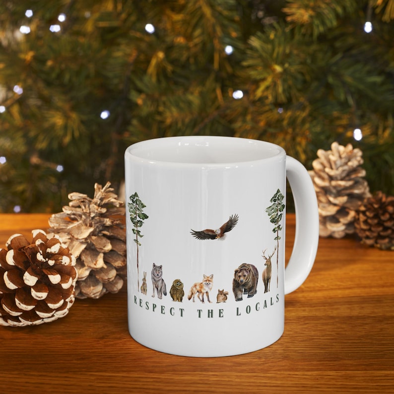 An 11 or 15 oz white ceramic coffee mug with a wildlife design on it that says RESPECT THE LOCALS - displaying forest animals such as rabbit, wolf, owl, fox, eagle, squirrel, bear, deer, buck. Great gift for a naturalist or wildlife rescue lover