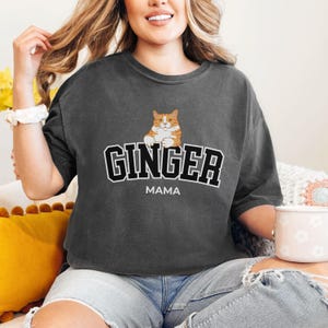 May include: A dark gray t-shirt with a cartoon orange and white cat and the text "GINGER MAMA" in black.