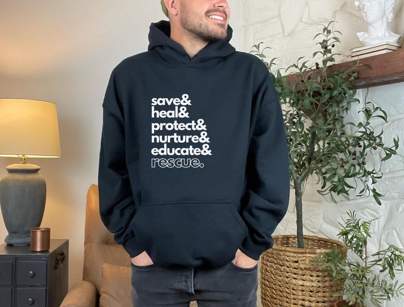 Peut inclure: Sweat-shirt &agrave; capuche noir avec texte blanc : "save & heal & protect & nurture & educate & rescue." Le sweat-shirt a une poche avant et une capuche &agrave; cordon. La personne porte un jean fonc&eacute;.