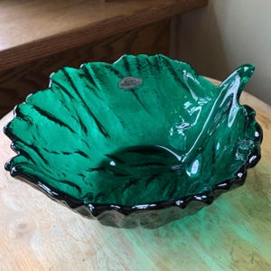May include: A vibrant green glass leaf-shaped bowl. The bowl has a textured surface with dark accents, and a scalloped edge. The bowl is likely a decorative piece, perfect for displaying small items or as a centerpiece.