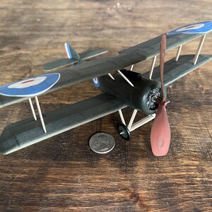 May include: A model of a green and brown biplane with a red propeller. The plane has a blue and white roundel on each wing.