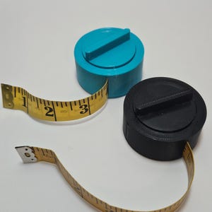 Pode incluir: Duas fitas métricas retráteis, uma preta e outra azul, com fita amarela. As fitas métricas têm uma forma redonda e compacta.