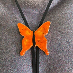 May include: Orange butterfly pendant necklace with a black suede cord.