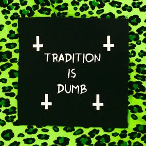 May include: A square black fabric patch featuring the white text TRADITION IS DUMB centered on the surface. Four white inverted crosses are positioned at each corner of the text. The patch is placed against a bright neon green leopard print fabric.