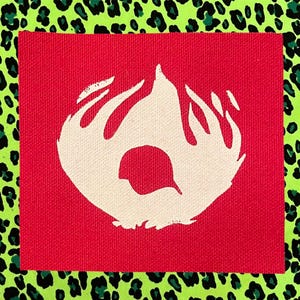 May include: A square fabric patch featuring a bright red background with a central off-white graphic of two hands cupped together, framing a small bird silhouette. The patch is set against a vibrant lime green and black leopard print background.