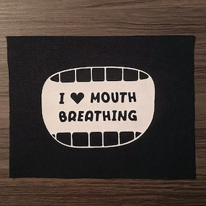 May include: Black rectangular patch with a white graphic of a mouth and the words "I ♥ MOUTH BREATHING" in black. The patch has a white border around the mouth graphic.