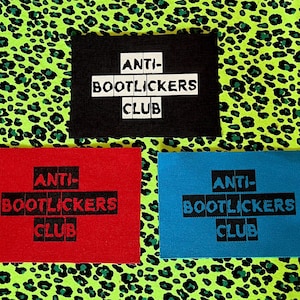 May include: Three rectangular patches with the text "ANTI-BOOTLICKERS CLUB" in a bold, blocky font. The patches are black, red, and blue, set against a neon green leopard print background.