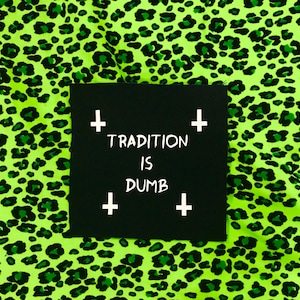 May include: Black patch with white text that reads "TRADITION IS DUMB" with a white cross on each corner. The patch is on a green and black leopard print fabric.