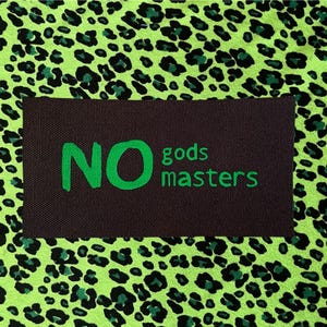 May include: A rectangular black fabric patch featuring the green text NO gods masters, centered on a vibrant lime green and black leopard print background. The patch has a woven texture and is positioned flat against the patterned fabric surface.
