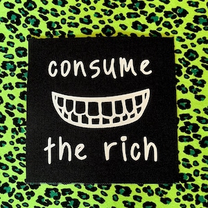 May include: A black square patch with the words "consume the rich" in white, above a white cartoon smile. The background is a neon green leopard print with dark green spots.