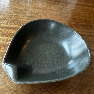 May include: A dark gray ceramic serving dish with a unique, slightly curved shape. The dish has a speckled, textured surface.