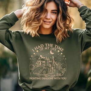 Op de afbeelding: Groen sweatshirt met een grafische print van een kasteel, maan en sterren. De tekst luidt "Ik had de tijd van mijn leven om draken met je te bevechten."