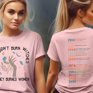 May include: Pale pink t-shirt featuring the slogan "THEY DIDN'T BURN WITCHES THEY BURNED WOMEN" with a hand and floral graphic. The back of the tee lists women's rights milestones from 1900 to 2024.