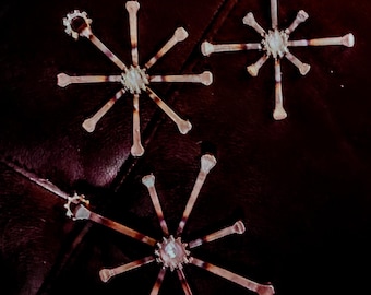 Puede incluir: Tres adornos de copo de nieve de metal con un acabado rústico martillado. Cada copo de nieve tiene un centro en forma de estrella y ocho puntas.