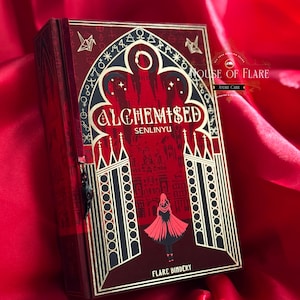K&ouml;nnte beinhalten: Ein dekoratives Buch mit rotem und goldenem Einband, mit dem Titel "ALCHEMISED" und gotischen Illustrationen. Das Design umfasst eine Figur-Silhouette und architektonische Details. Das Buch liegt auf rotem Satinstoff.