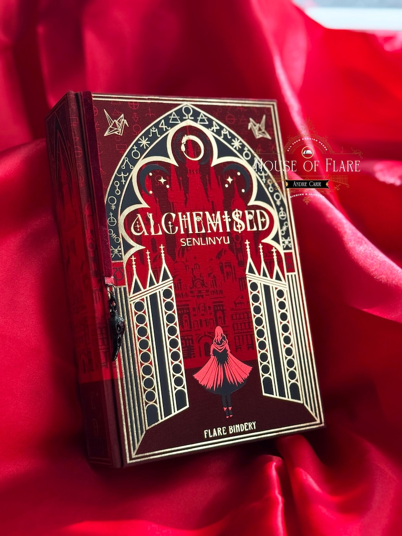 K&ouml;nnte beinhalten: Ein dekoratives Buch mit rotem und goldenem Einband, mit dem Titel "ALCHEMISED" und gotischen Illustrationen. Das Design umfasst eine Figur-Silhouette und architektonische Details. Das Buch liegt auf rotem Satinstoff.