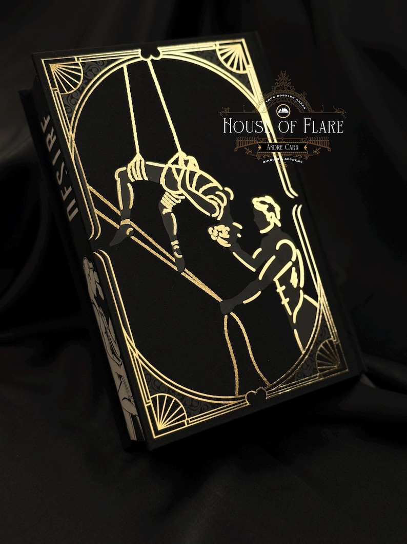 Może przedstawiać: Czarna książka ze złotymi detalami w stylu art deco i napisem "DESIRE" na grzbiecie. Okładka przedstawia złotą ilustrację dw&oacute;ch postaci. Książka nosi tytuł "HOUSE OF FLARE" i "ANDRE CARR".