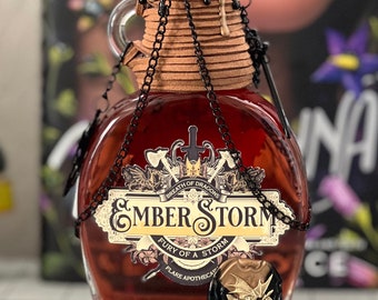 May include: A glass bottle with a cork stopper and a black chain. The bottle is filled with a dark red liquid and has a label that reads "Ember Storm, Breath of Dragons, Fury of a Storm, Flare Apothecary". The bottle is decorated with a gold dragon shield.