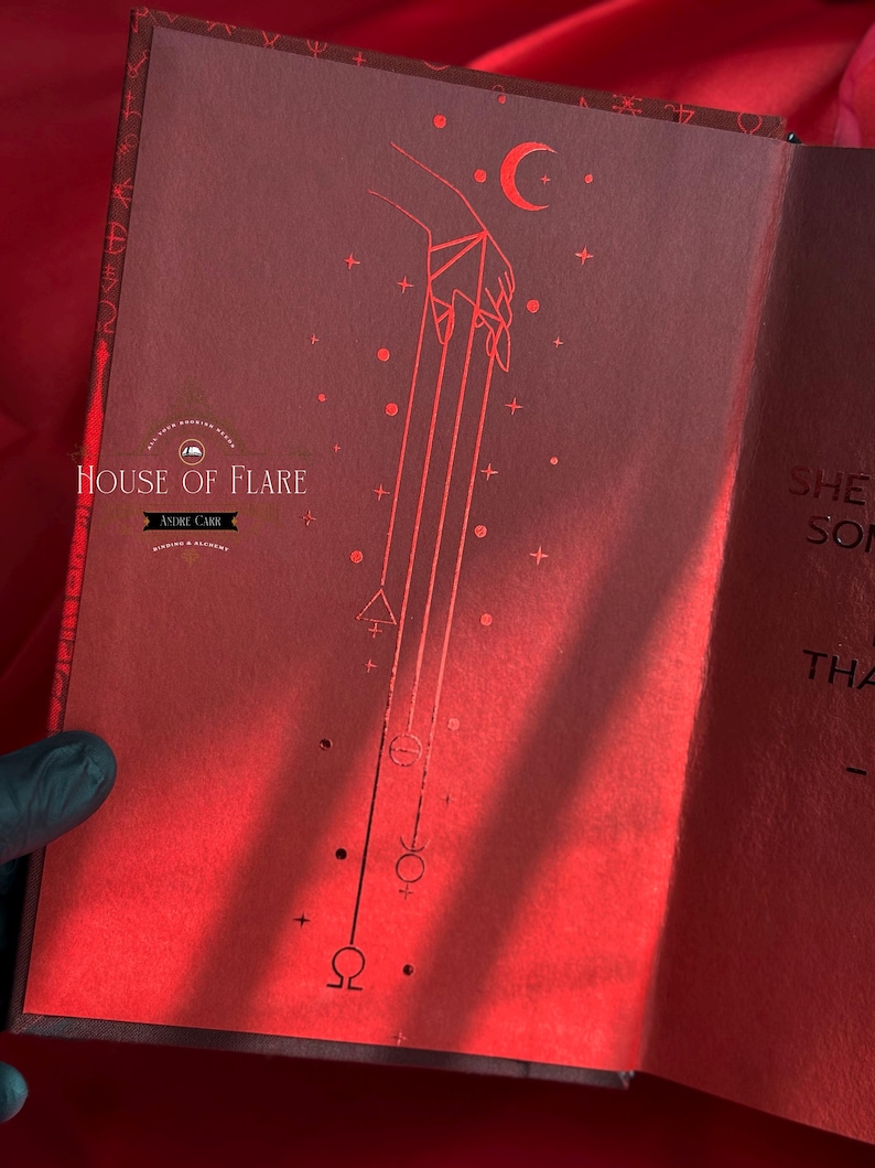 K&ouml;nnte beinhalten: Offenes Buch mit roten Seiten und einer detaillierten Illustration. Die linke Seite zeigt eine Hand mit Linien, einen Halbmond und Symbole. Das Buch tr&auml;gt die Aufschrift "HOUSE OF FLARE" und "ANDRE CARR".